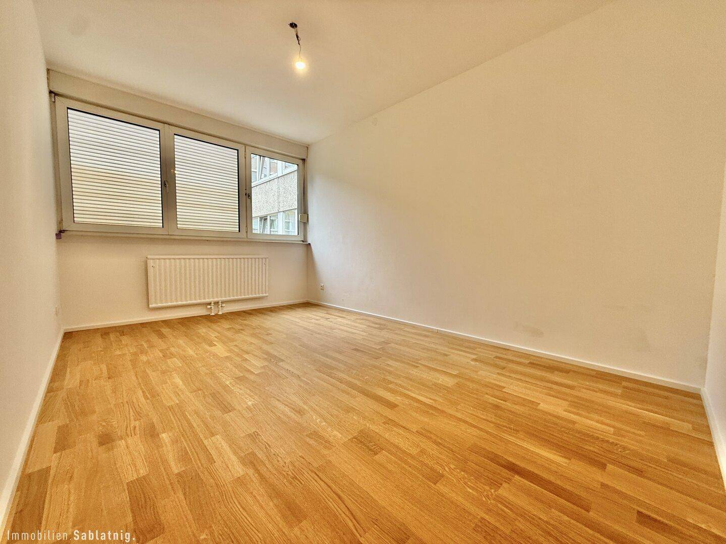 Geräumiges Schlafzimmer mit hellem Parkettboden und großen Fenstern für viel Tageslicht.