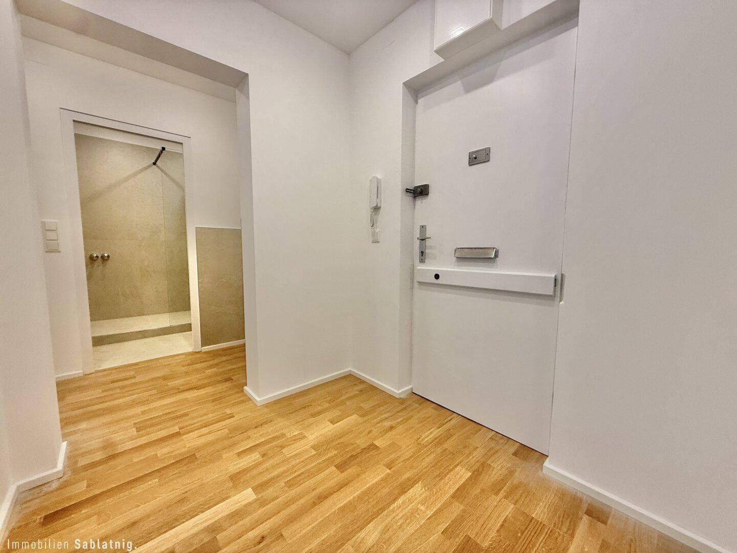 Heller Eingangsbereich mit Holzboden und Zugang zu einem modernen Badezimmer.