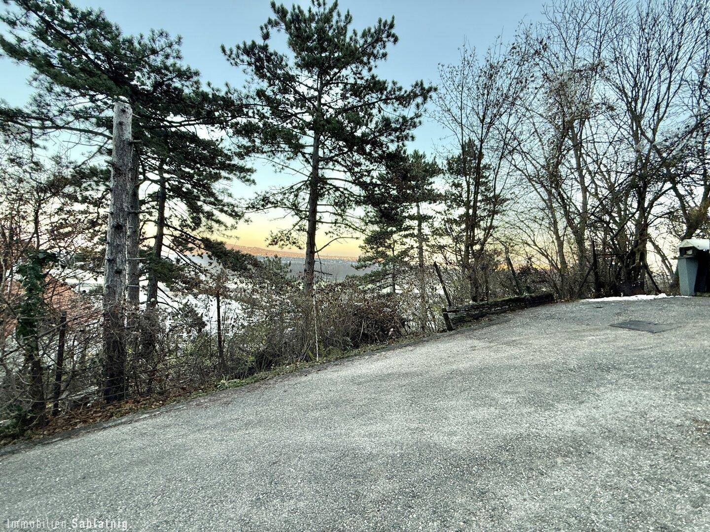 Schotterweg mit Bäumen und Sträuchern, der einen weiten Blick auf das Wasser und die Landschaft bietet.