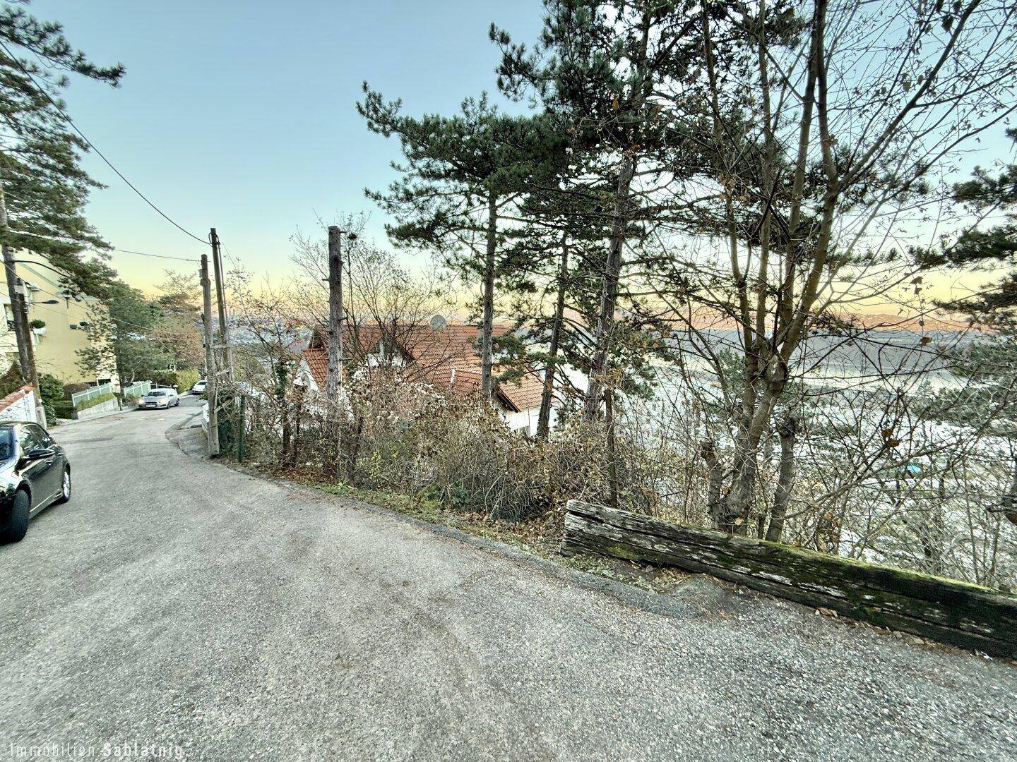 Kurviger Schotterweg mit parkendem Auto und Blick auf das Wasser durch die Bäume.