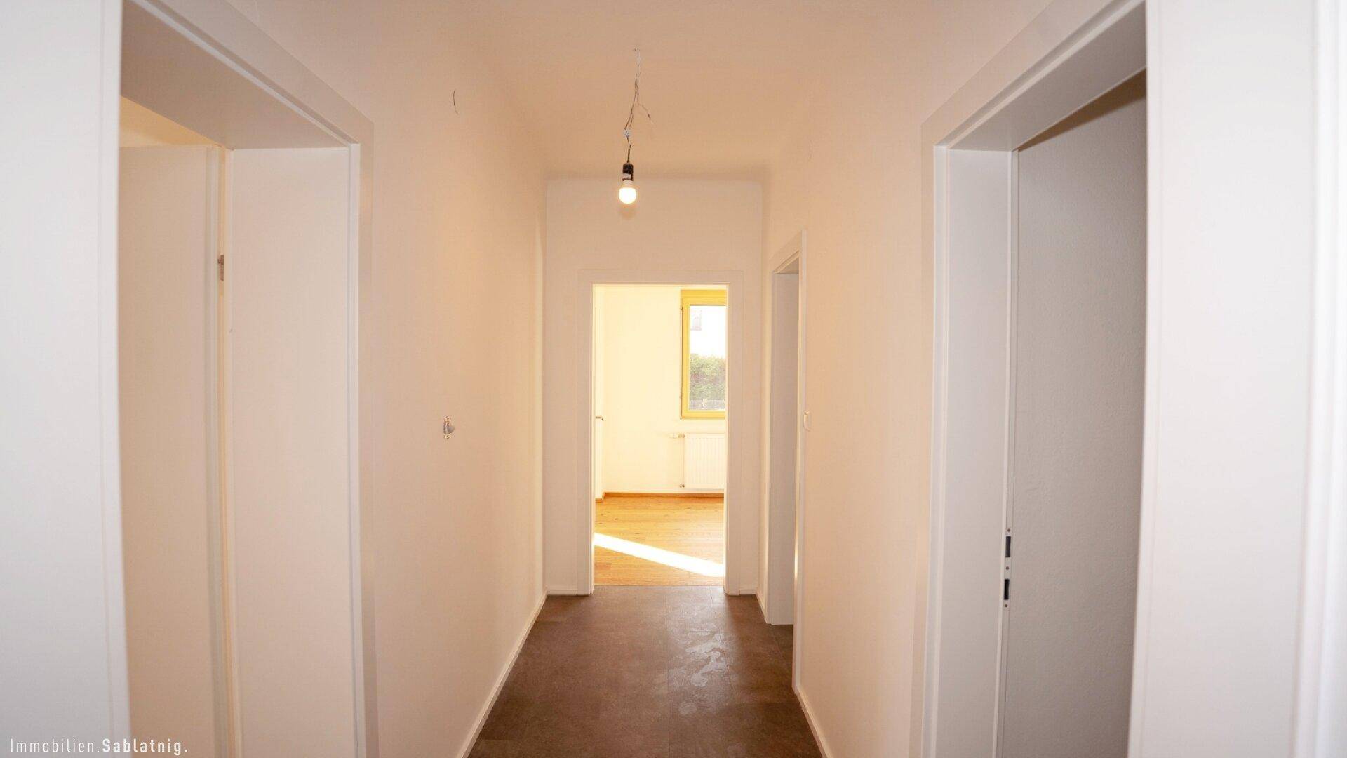 Heller Flur mit dunklem Fliesenboden und Zugang zu mehreren Zimmern.