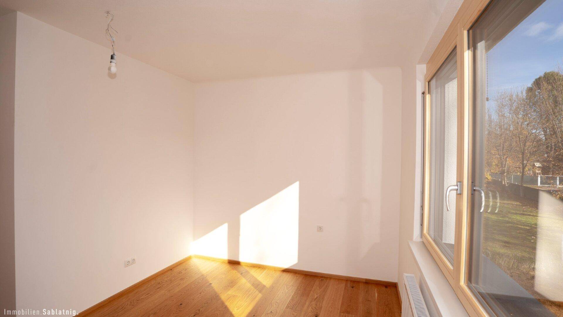 Helles Schlafzimmer mit Eichenparkettboden und großem Fenster mit Blick ins Grüne.