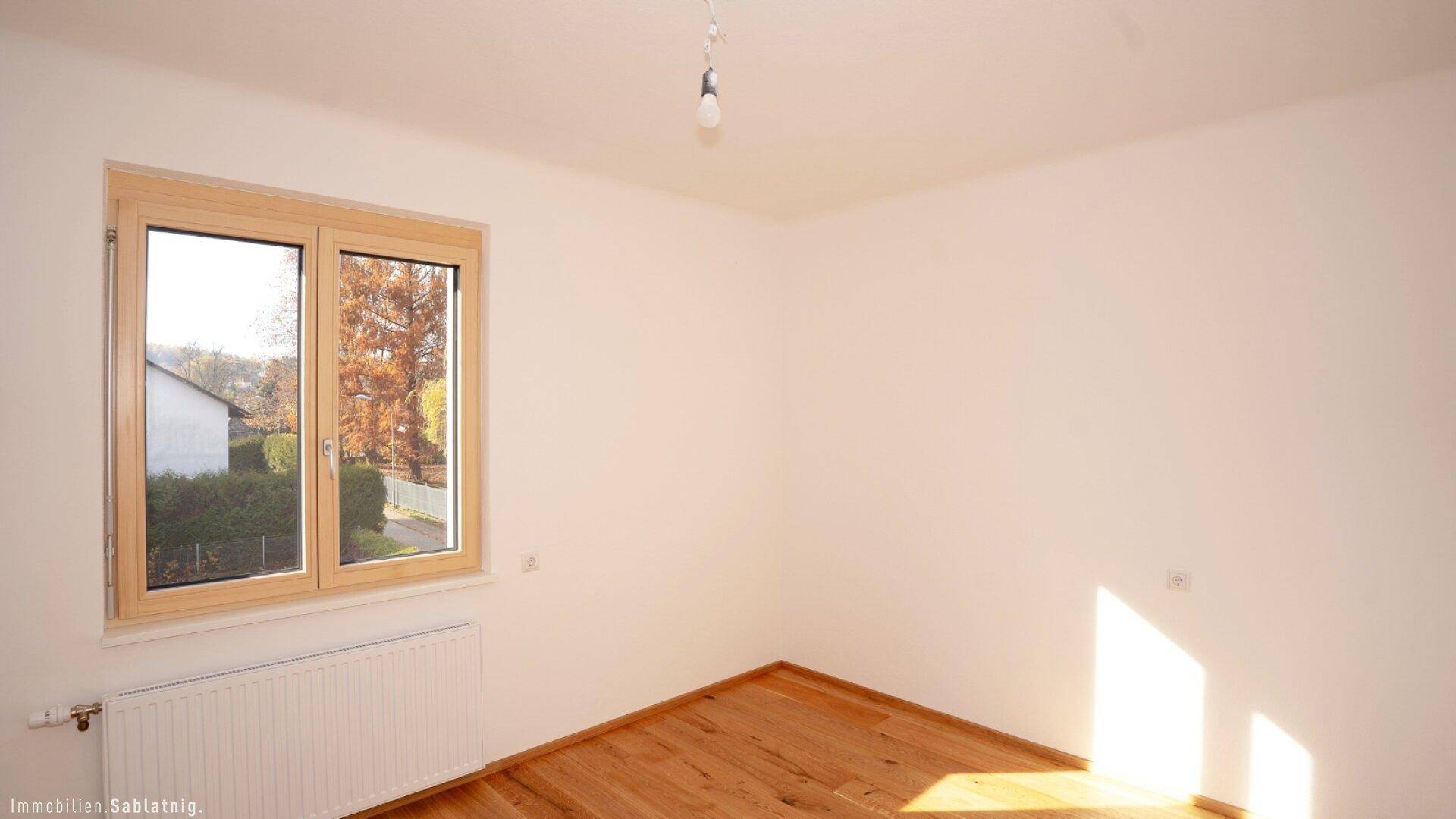 Geräumiges Schlafzimmer mit hellem Eichenparkett und einem Fenster mit Blick nach draußen.