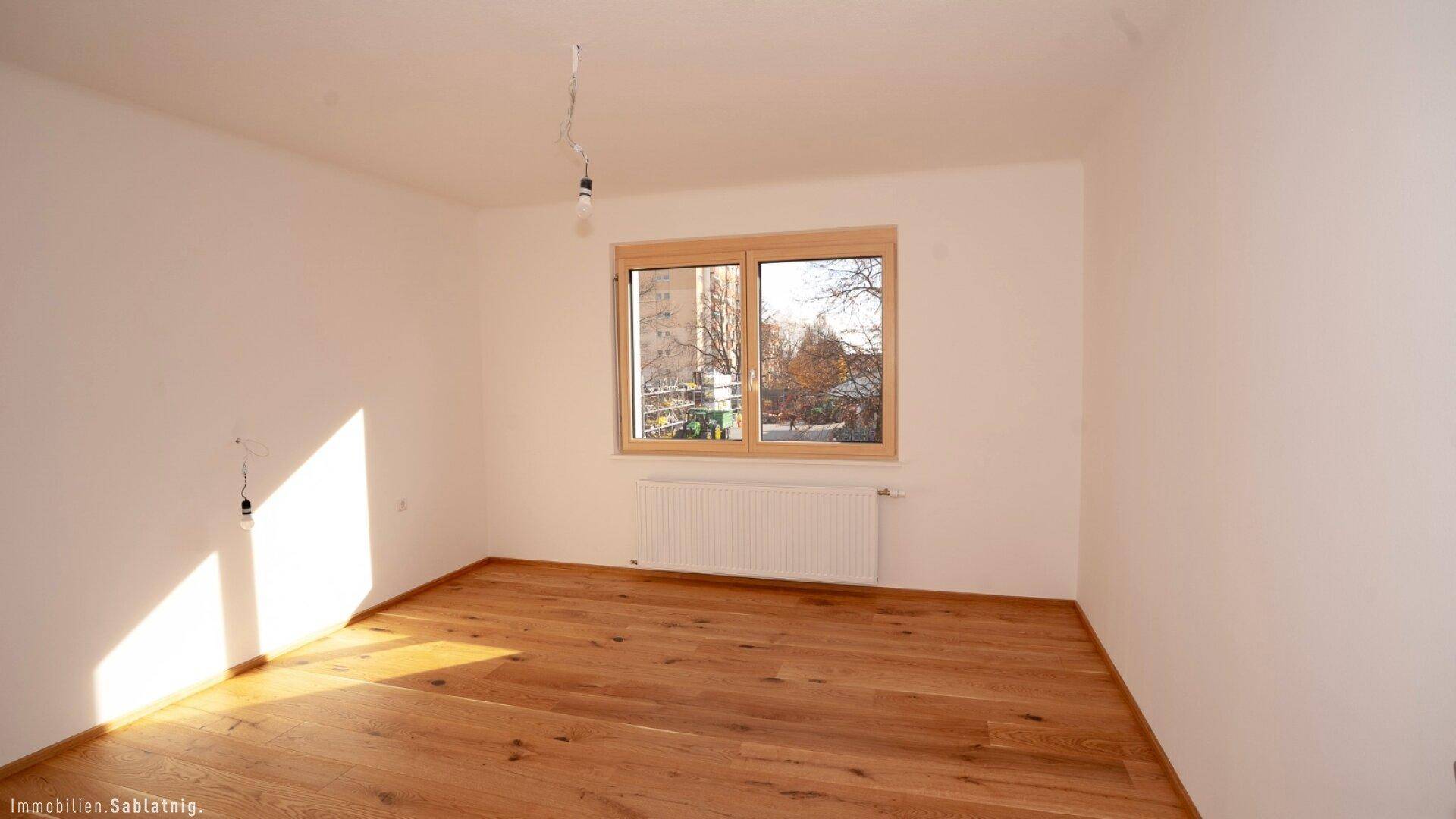 Helles Schlafzimmer mit Eichenparkettboden und großem Fenster, das viel Tageslicht hereinlässt.