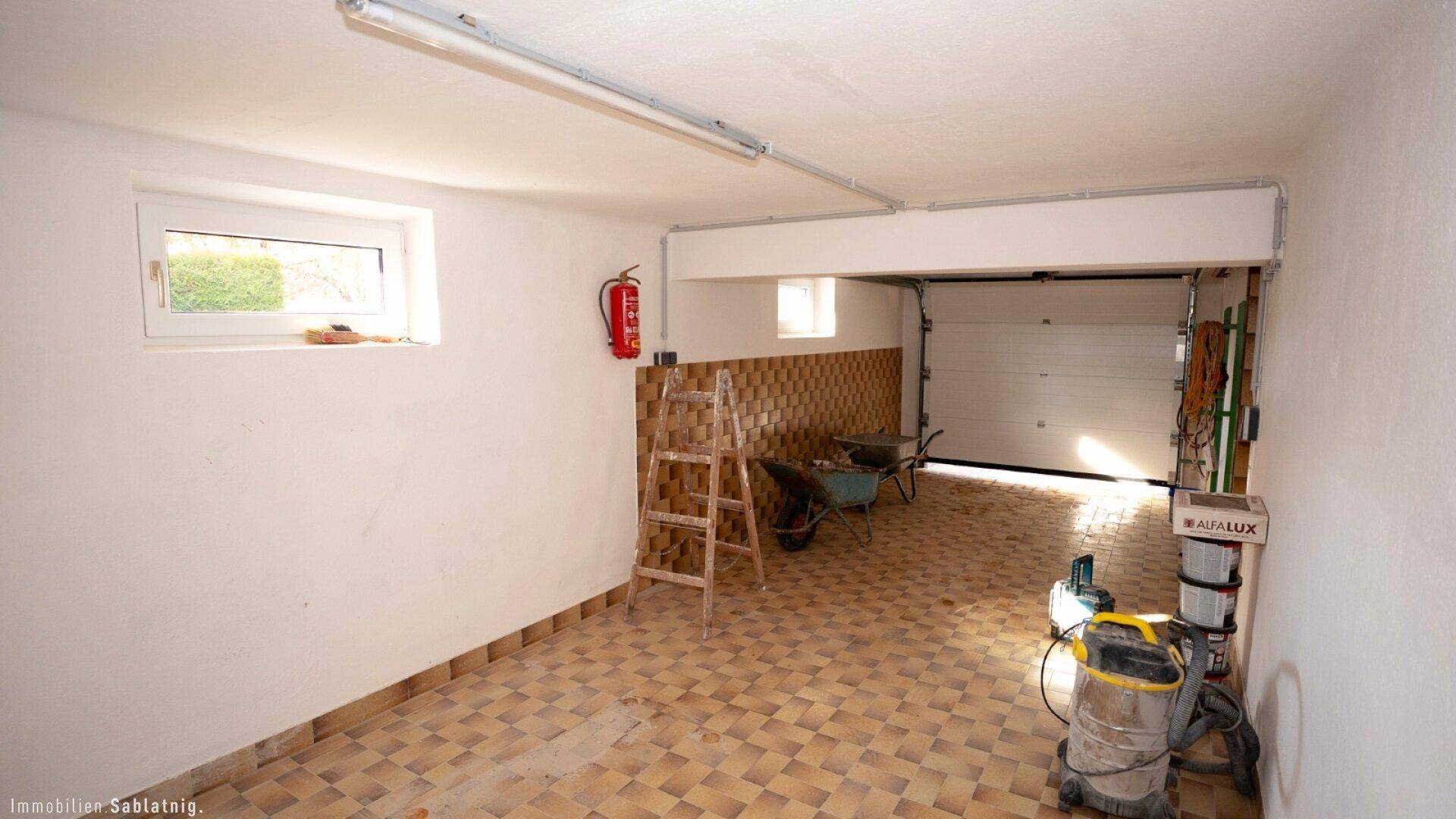 Geräumige Garage mit Fliesenboden und Rolltor, bietet Platz für Fahrzeuge und Lagerung.