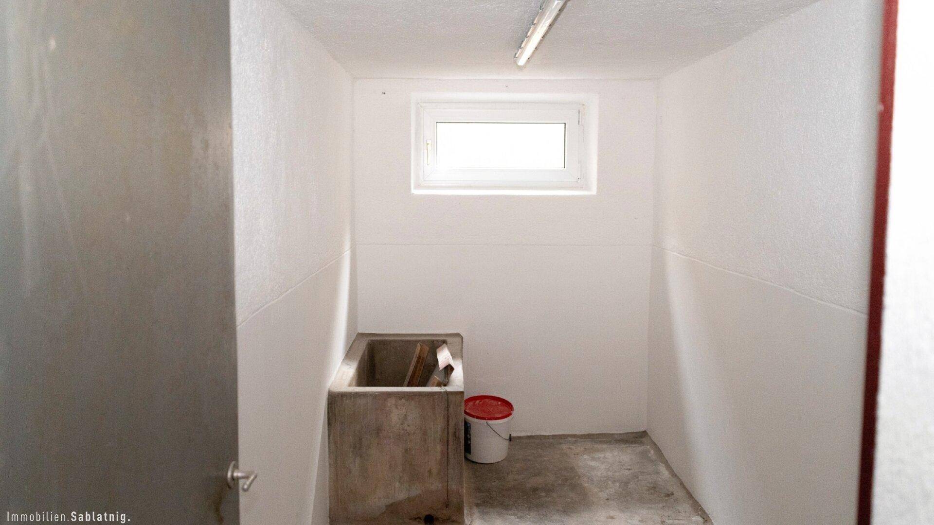 Einfacher Waschraum im Keller mit Waschbecken und Fenster.