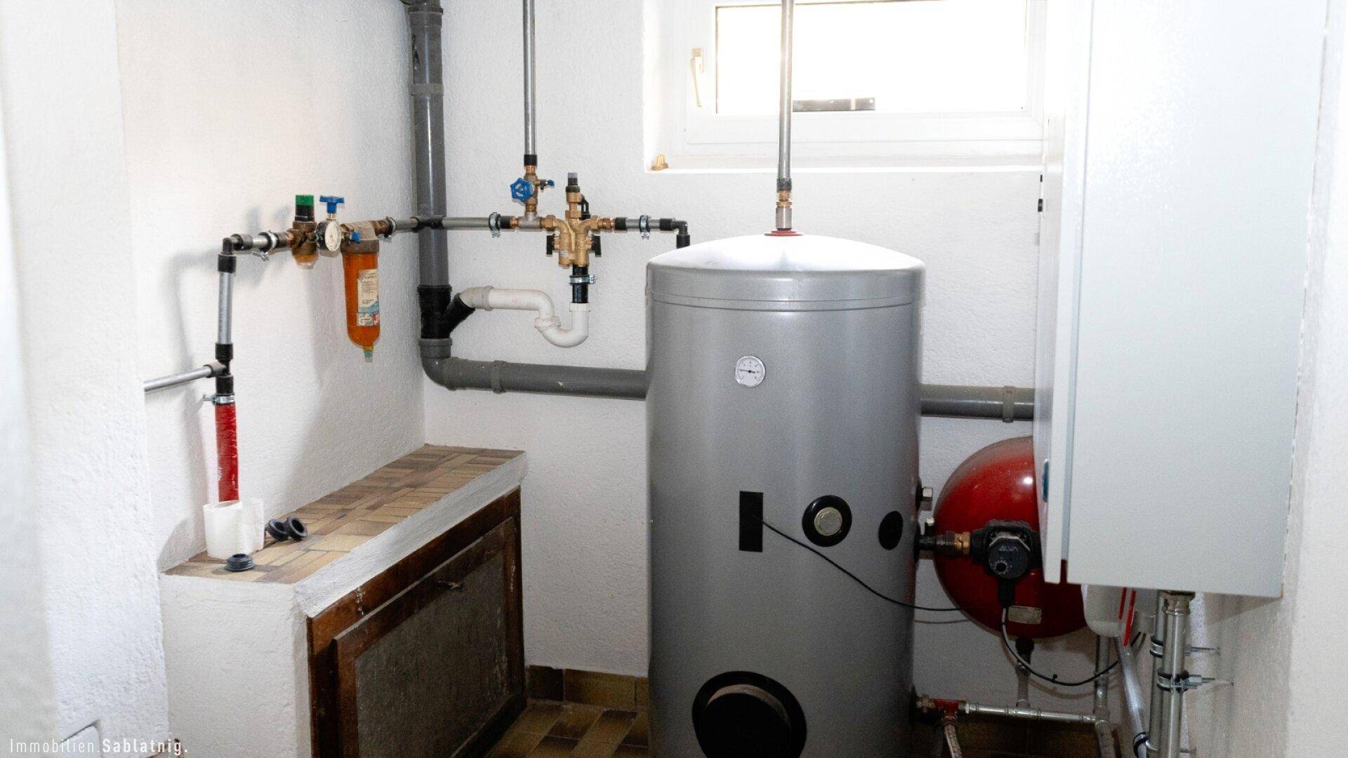 Heizungsraum im Keller mit Warmwasserspeicher und Fenster.