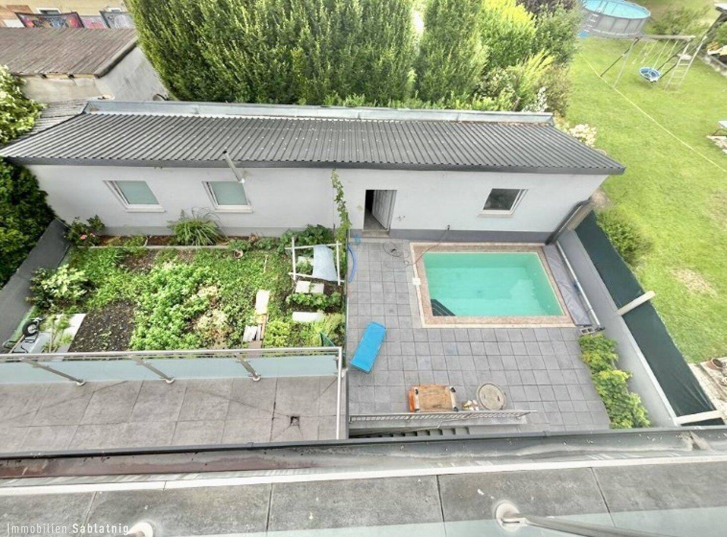 Gartenbereich mit Swimmingpool und gepflasterter Terrasse, umgeben von viel Grün.