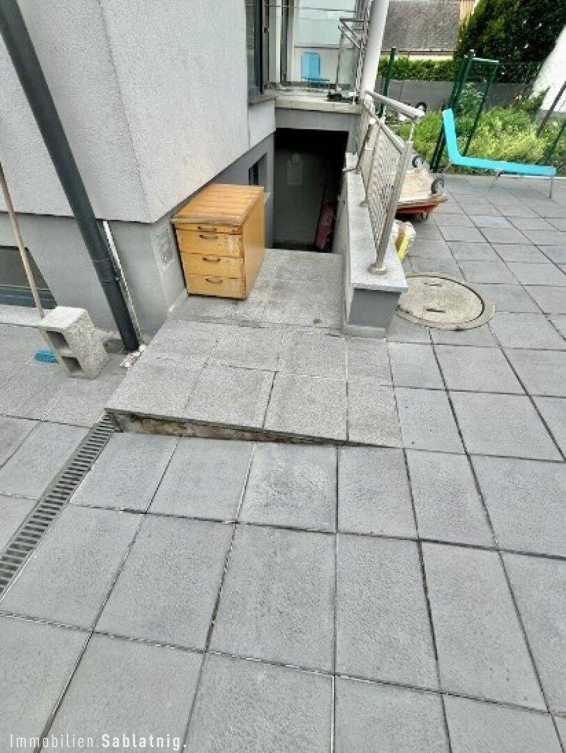 Eingangsbereich zum Untergeschoss mit Steinfliesen und einer kleinen Treppe.