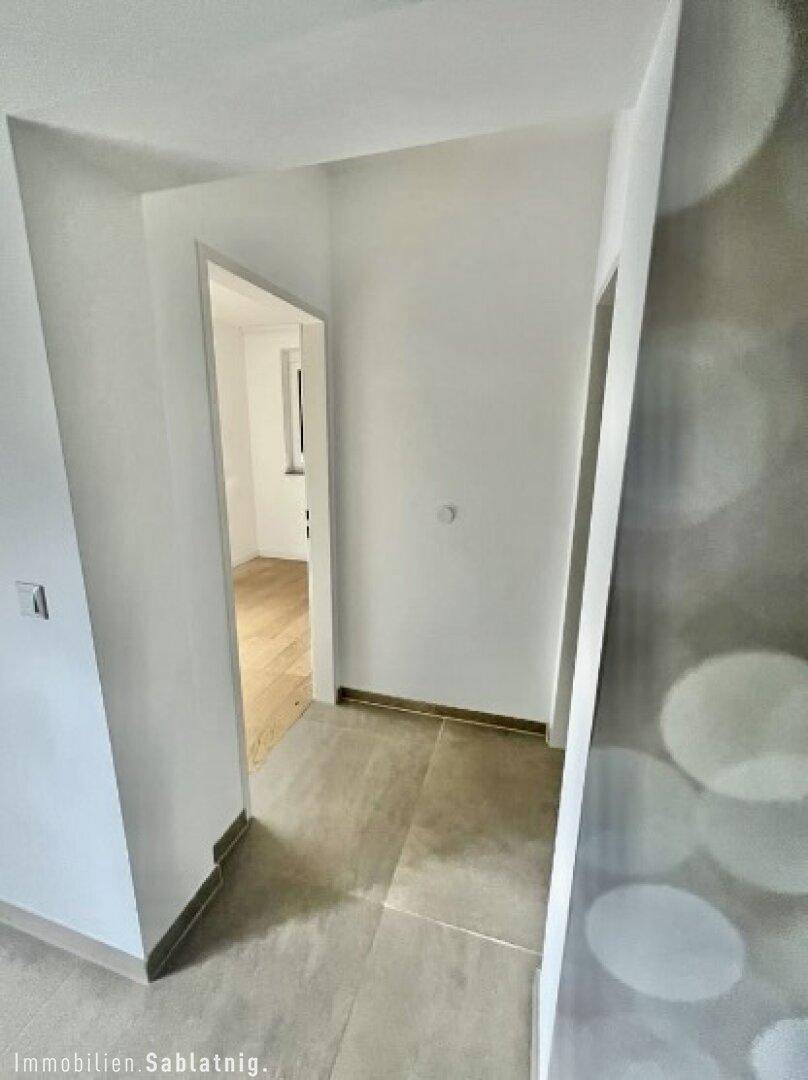 Heller Flur mit Fliesenboden, der zu einem Zimmer mit Holzboden führt.