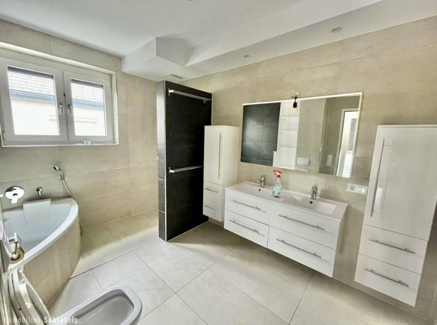 Geräumiges Badezimmer mit Doppelwaschbecken, Eckbadewanne und großen Fliesen.