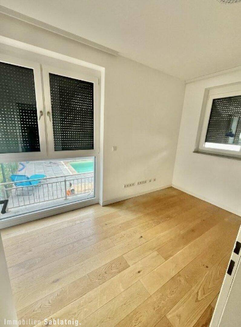 Schlafzimmer mit Holzboden und großem Fenster, bietet Blick auf den Poolbereich.