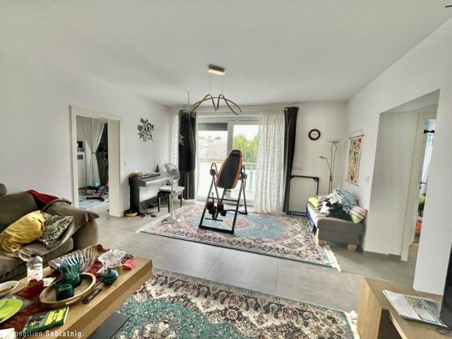 Gemütliches Wohnzimmer mit Teppichen, großen Fenstern und Zugang zum Balkon.