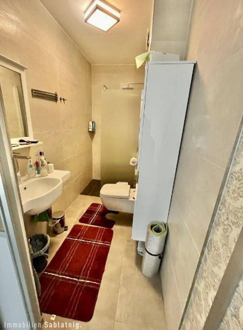 Kleines Badezimmer mit Dusche, Waschbecken und Wand-WC, funktional eingerichtet.