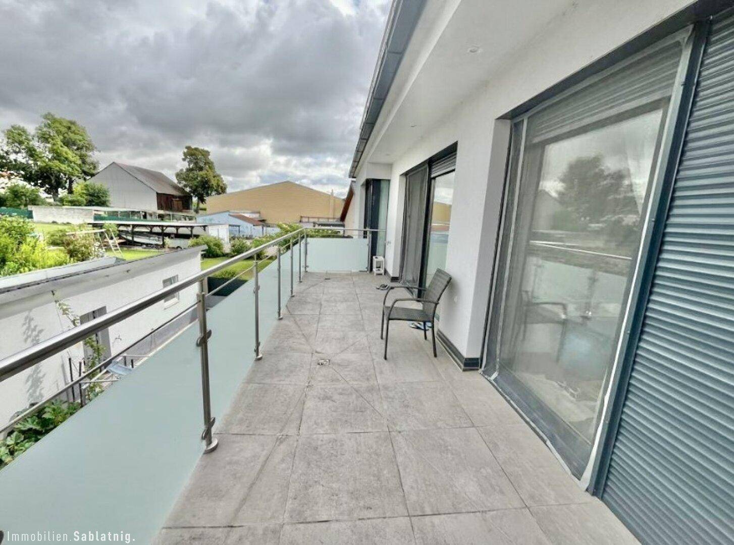 Langer Balkon mit Fliesenboden und Glasgeländer, bietet Platz für Sitzgelegenheiten.