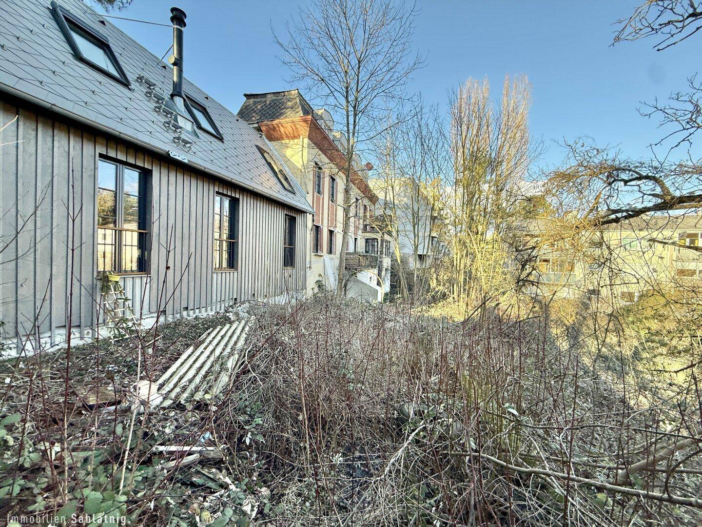 Seitenansicht eines Gebäudes mit Holzfassade und Dachfenstern, umgeben von Vegetation.
