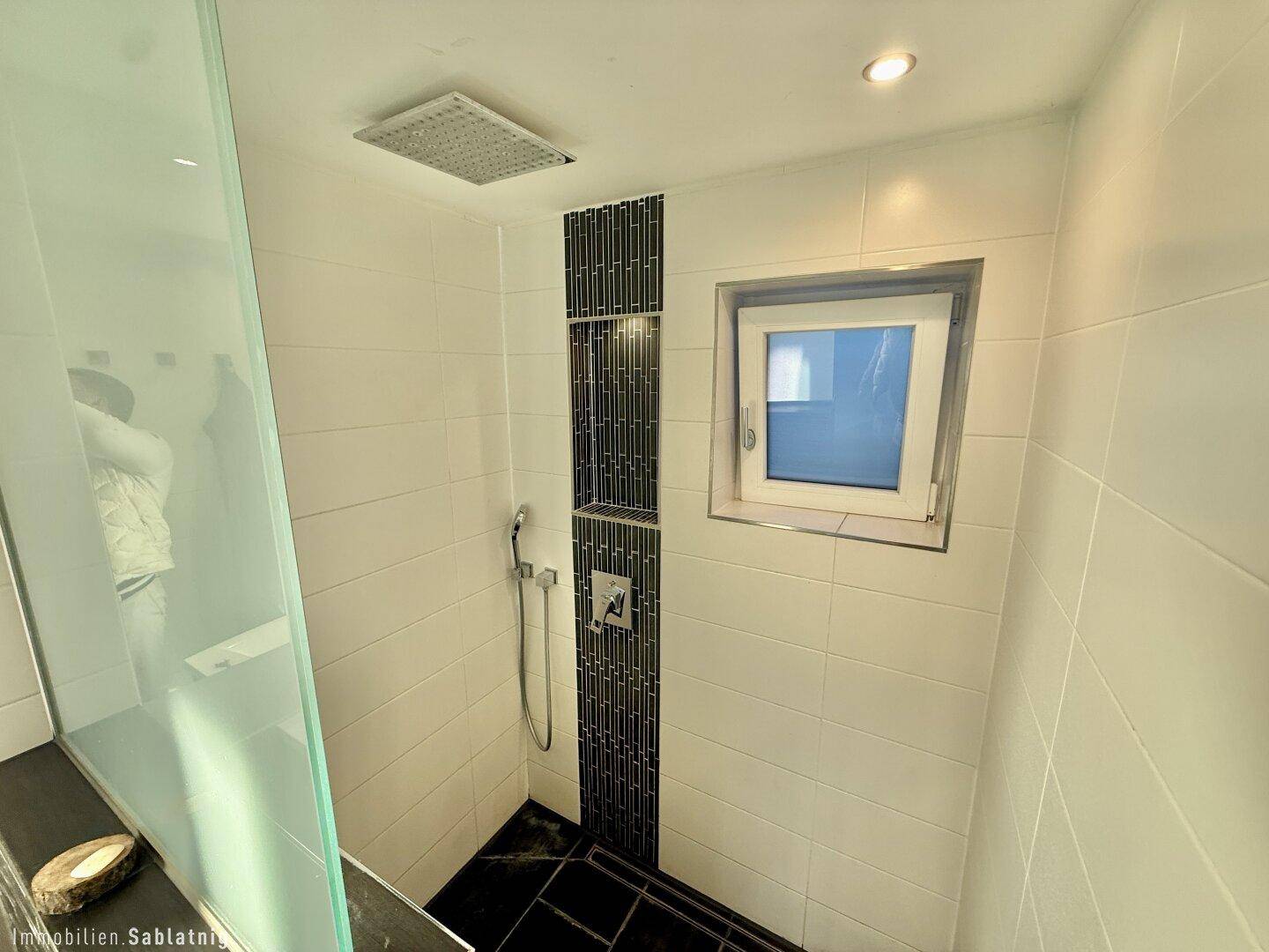 Moderne Dusche mit Regenduschkopf, Fliesen und Fenster für Tageslicht.