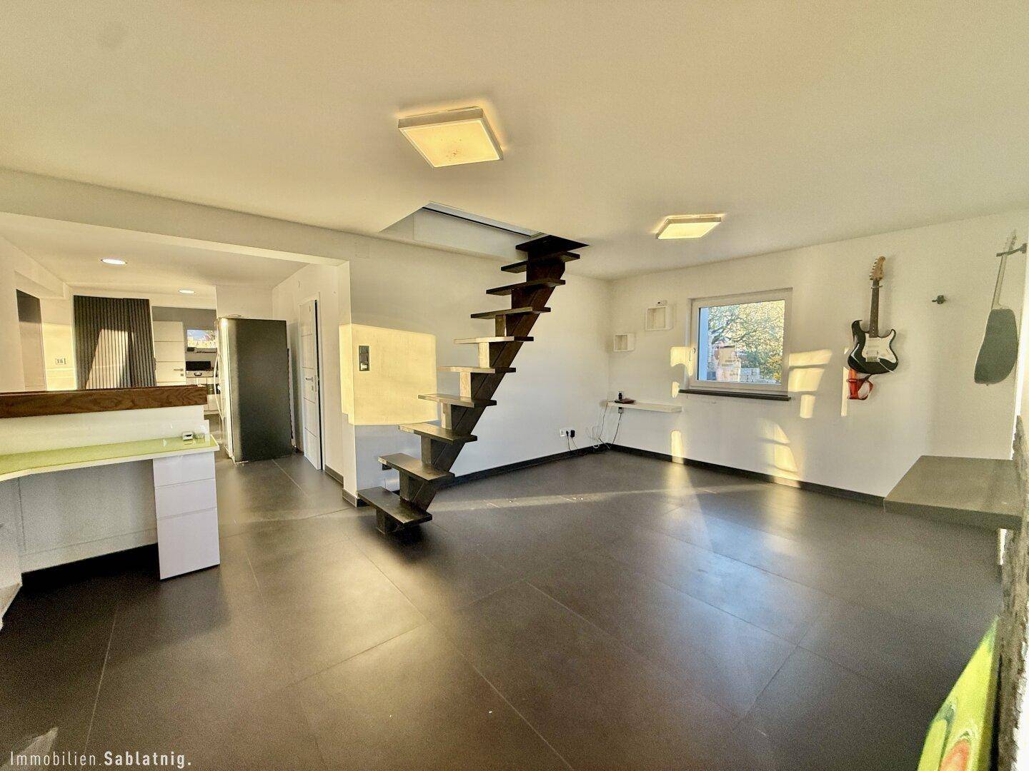 Heller Wohnbereich mit offener Treppe, großen Fenstern und viel Tageslicht.