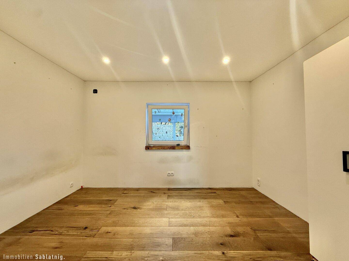 Helles Zimmer mit Holzboden und einem Fenster, bereit zur individuellen Gestaltung.
