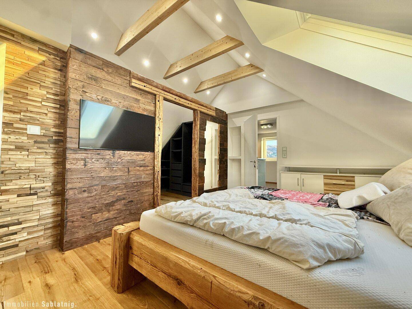 Schlafzimmer im Dachgeschoss mit Holzwand, Holzbalken und integriertem Kleiderschrank.