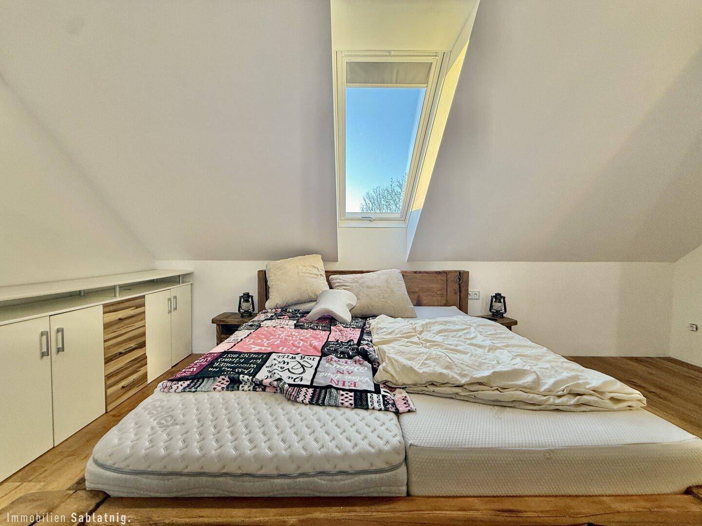 Helles Schlafzimmer im Dachgeschoss mit Holzbett und Dachfenster.