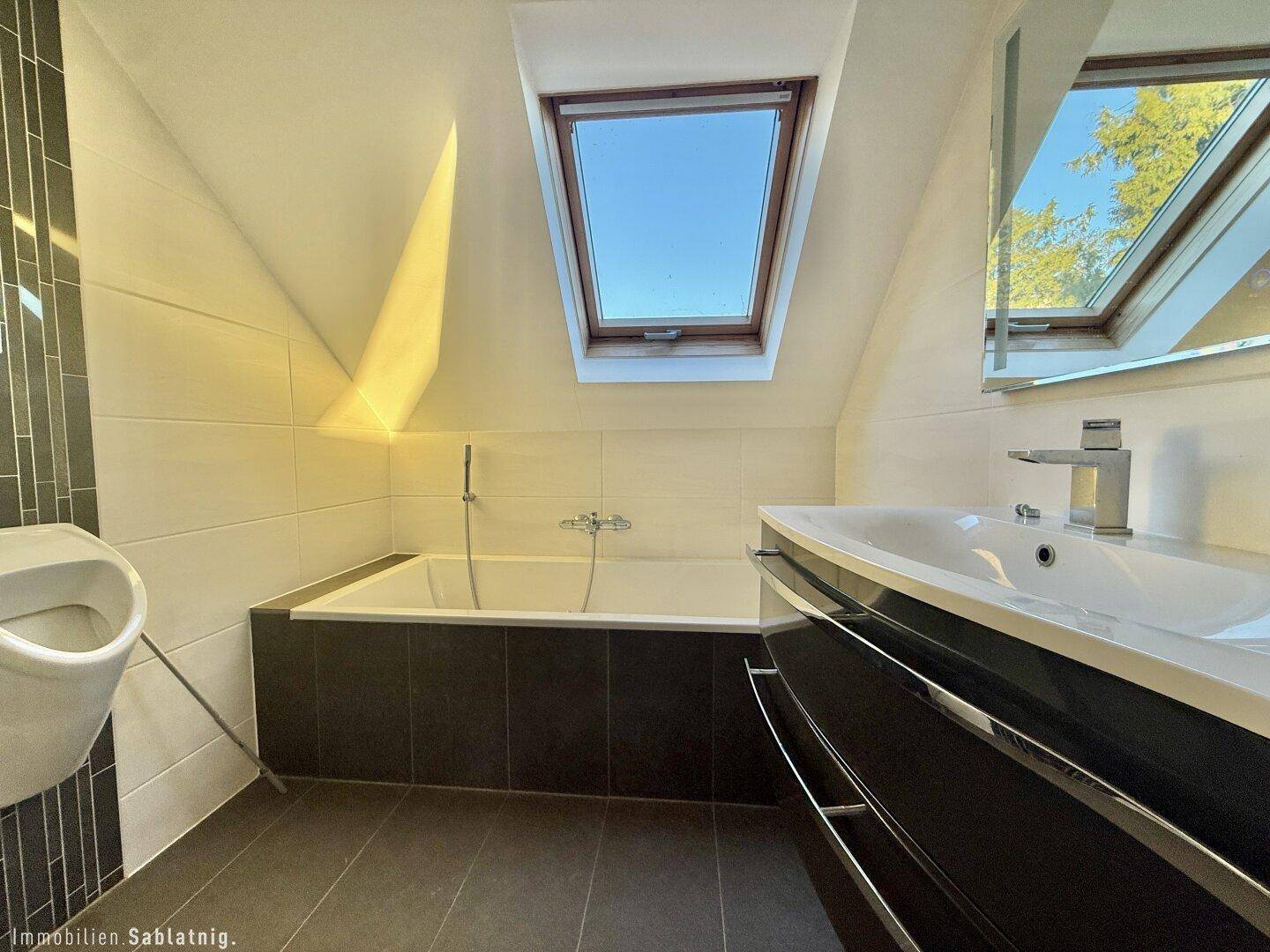 Modernes Badezimmer im Dachgeschoss mit Badewanne, Urinal und Dachfenster.