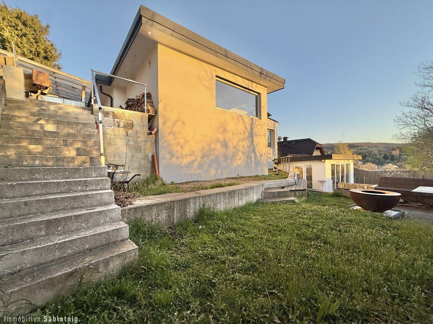 Außenansicht des Hauses mit Treppen und Gartenbereich bei Sonnenuntergang.