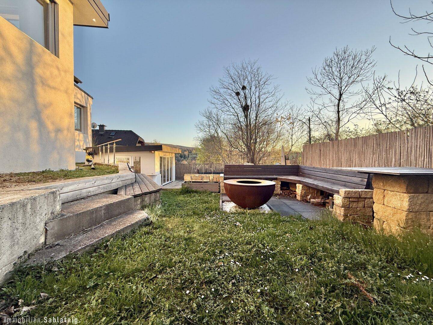 Gartenbereich mit Feuerstelle und Sitzgelegenheiten, umgeben von Natur.