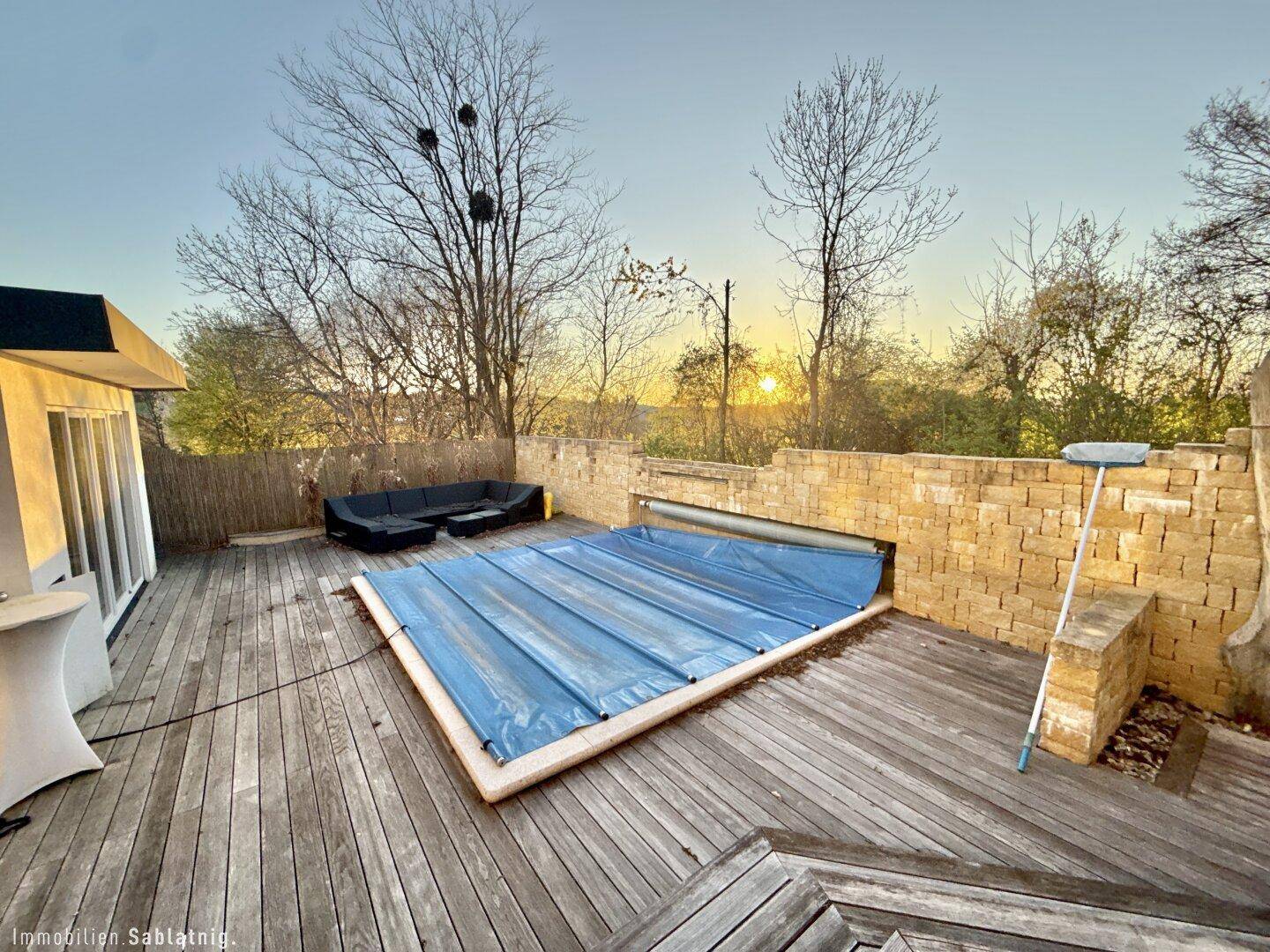 Große Holzterrasse mit überdachtem Pool und Sitzgelegenheiten im Freien.