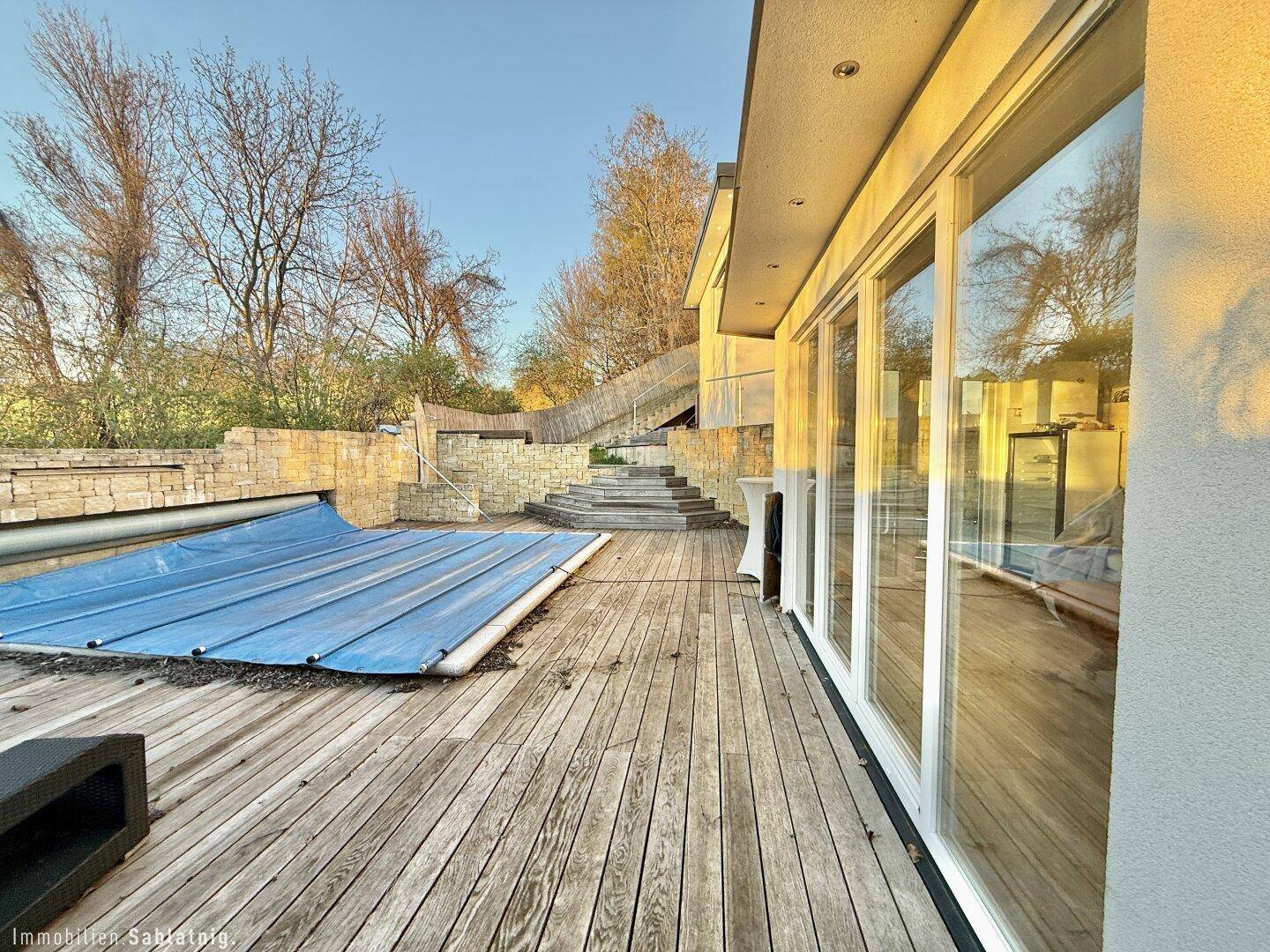 Große Holzterrasse mit Zugang zum Haus durch Panoramafenster.