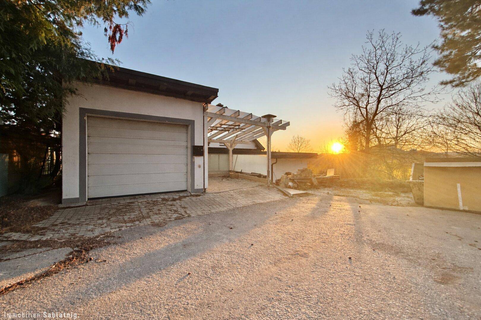Außenansicht der Garage mit Carport und Einfahrt bei Sonnenuntergang.