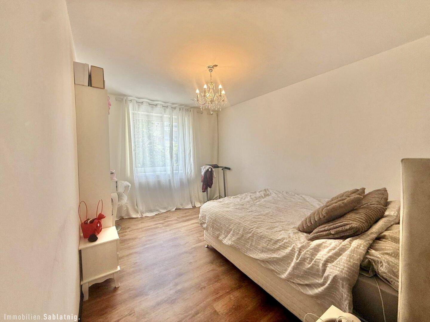 Schlafzimmer mit Einzelbett, Parkettboden und Fenster mit Vorhängen.