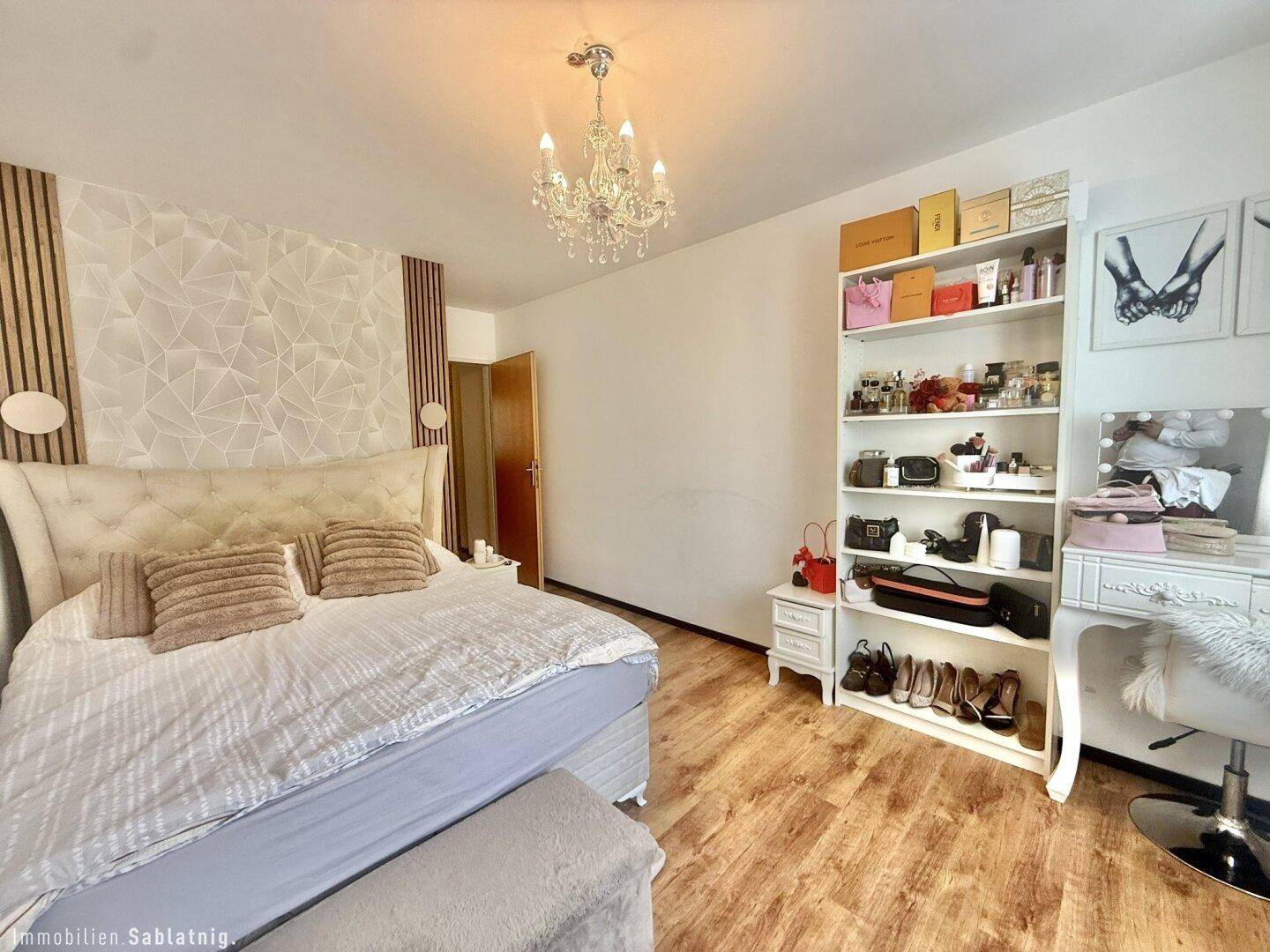 Helles Schlafzimmer mit großem Bett, offener Regalwand und Schminktisch.