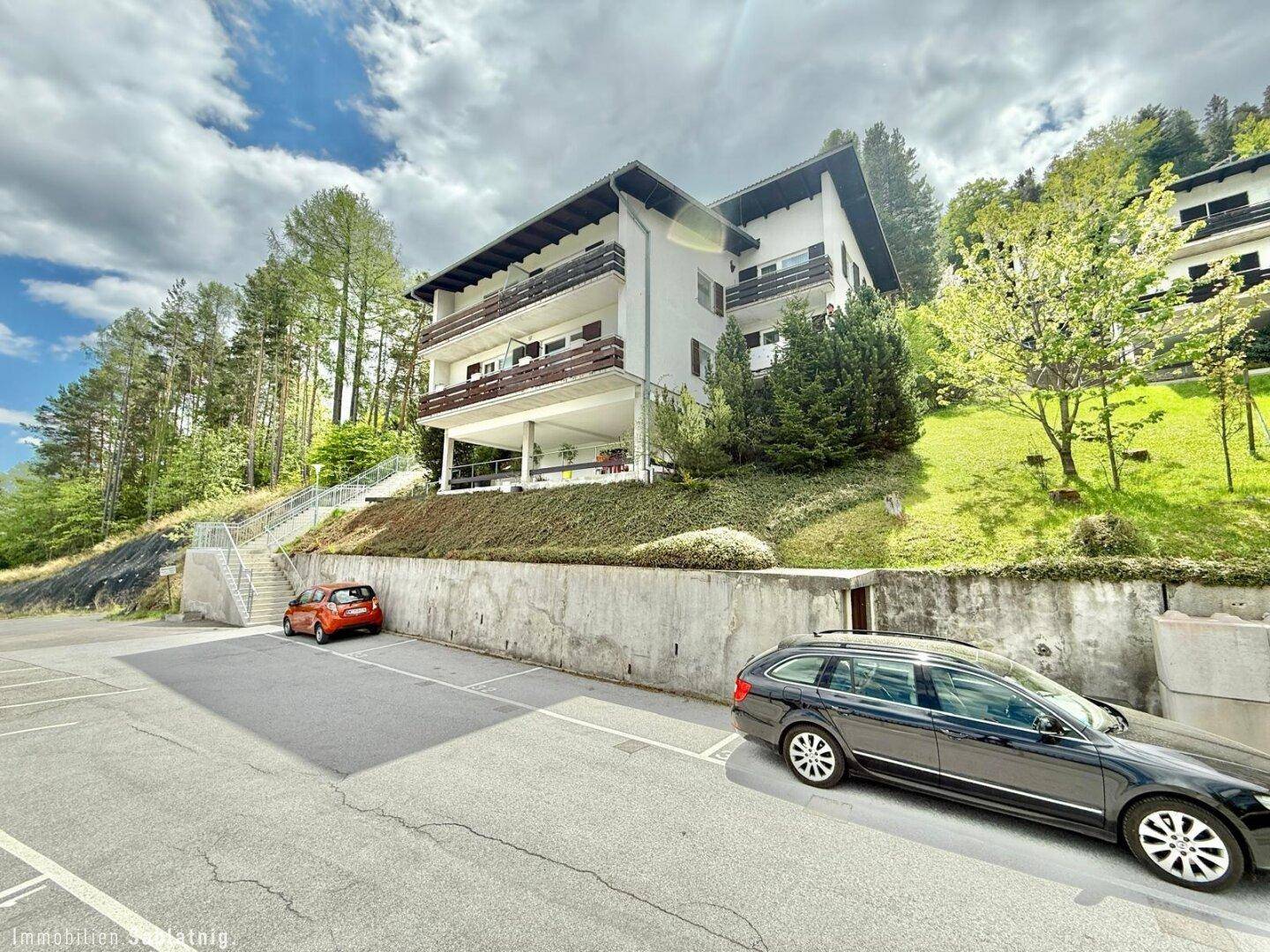 Mehrfamilienhaus in Hanglage mit Balkonen und Außenparkplätzen.