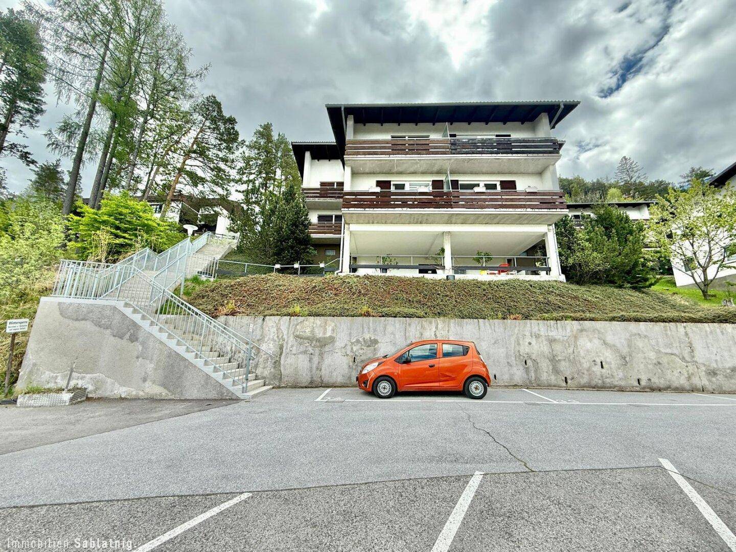 Wohngebäude in idyllischer Hanglage mit mehreren Balkonen und Parkplätzen.