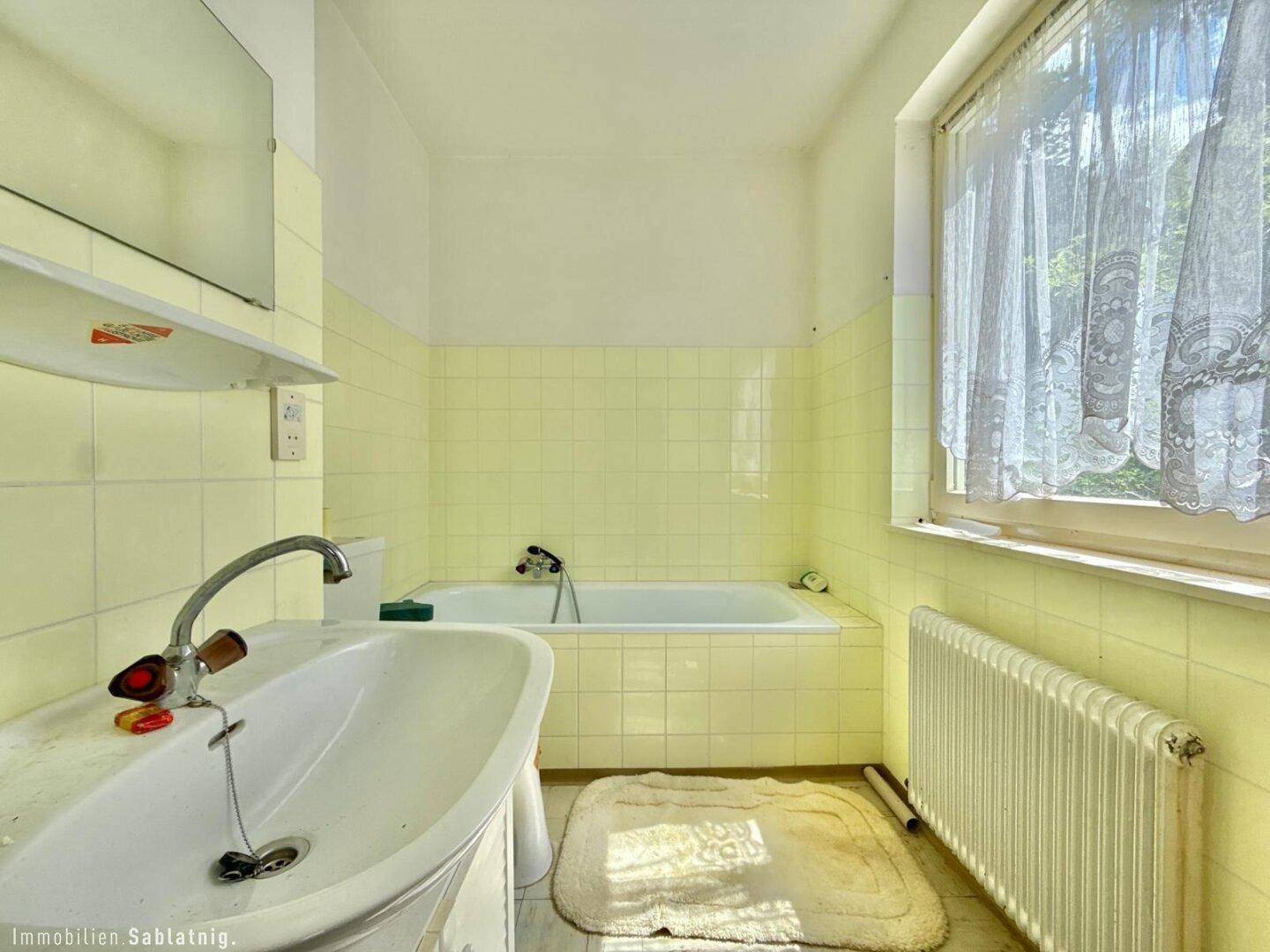 Helles Badezimmer mit gelben Fliesen, Badewanne und großem Fenster.