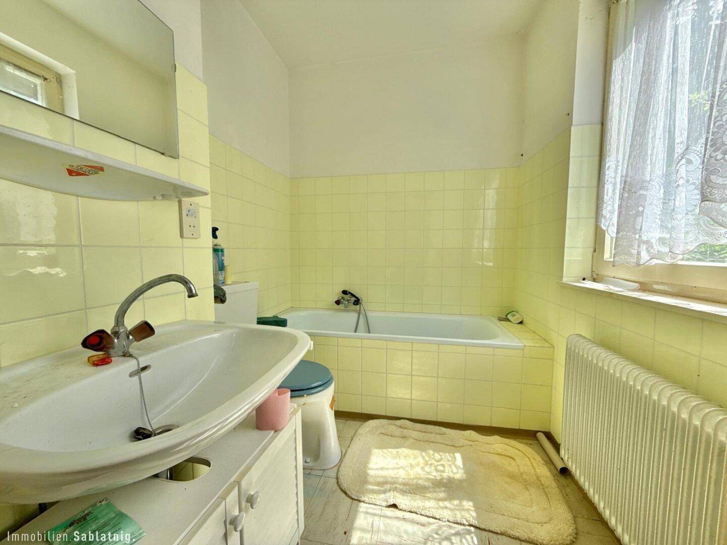 Badezimmer mit gelben Fliesen, Badewanne, Waschbecken und Fenster.