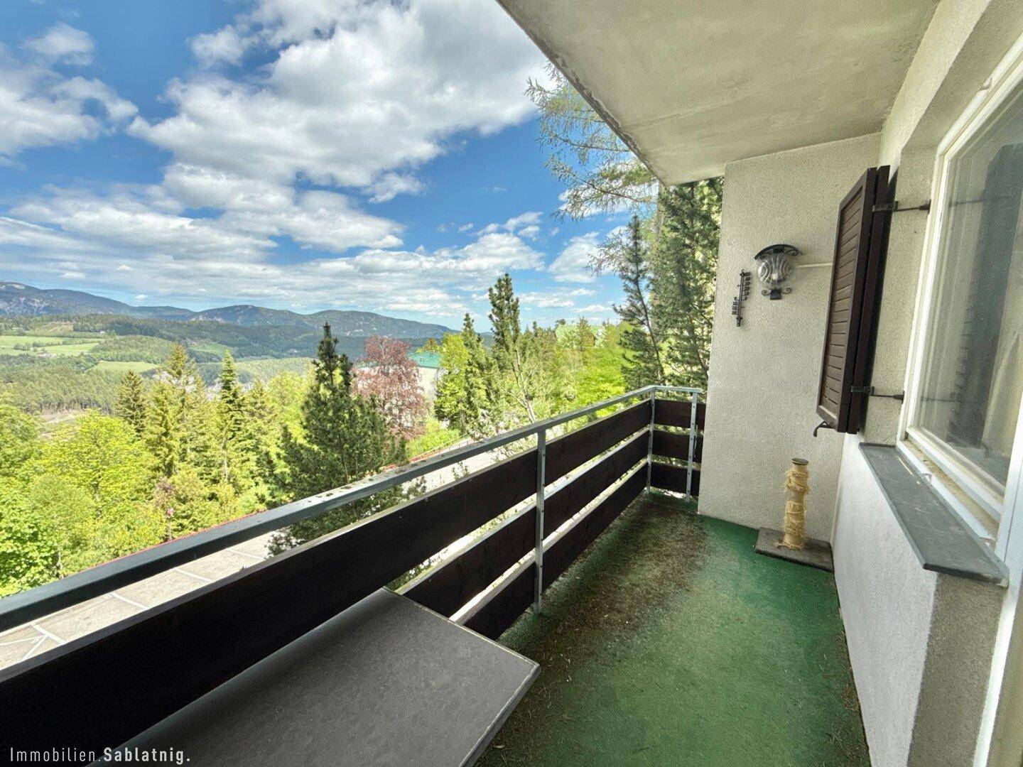 Sonniger Balkon mit Panoramablick auf die umliegende Berglandschaft und Wälder.