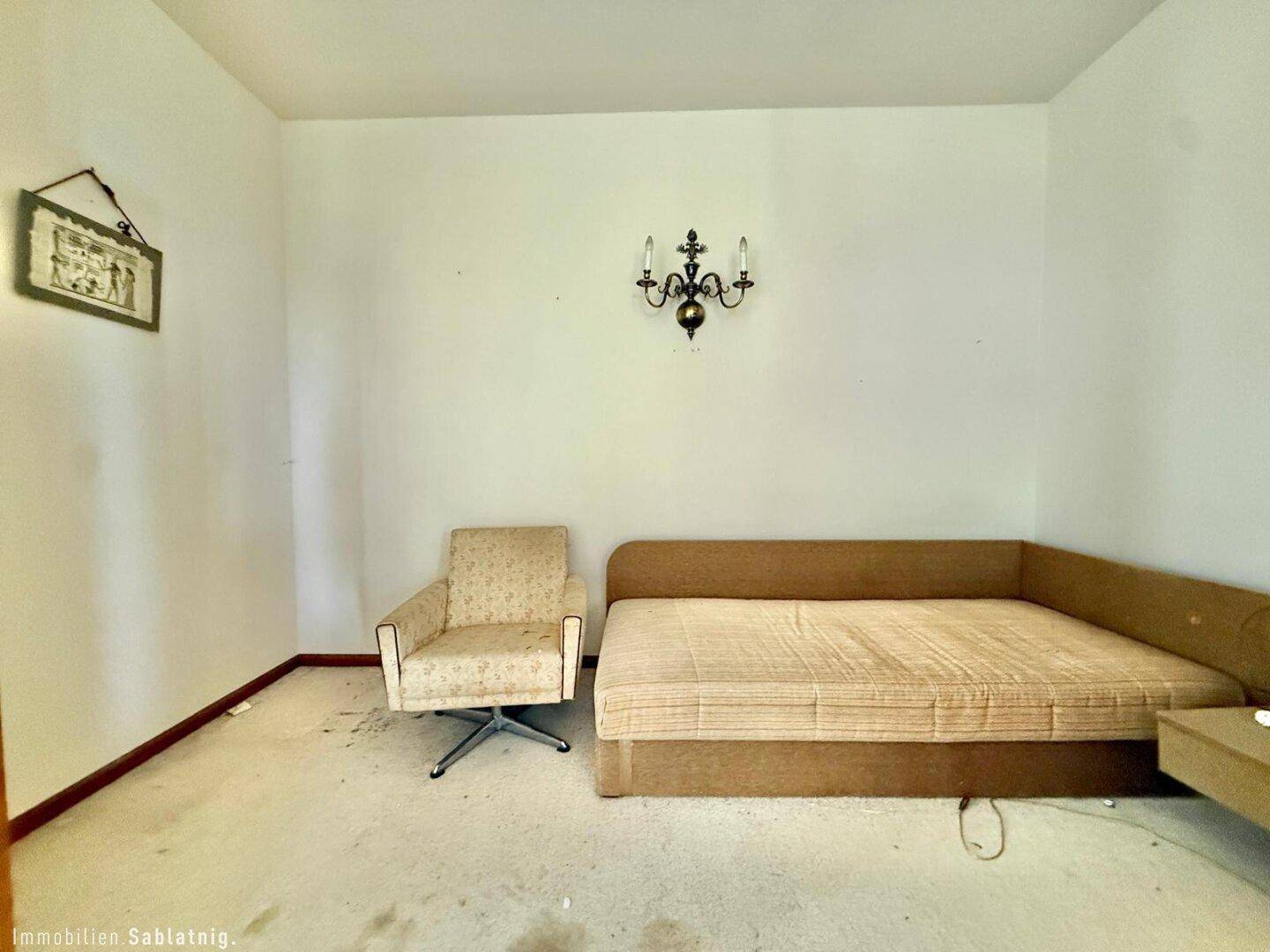 Schlafzimmer mit Einzelbett, Sessel und Wandleuchte.