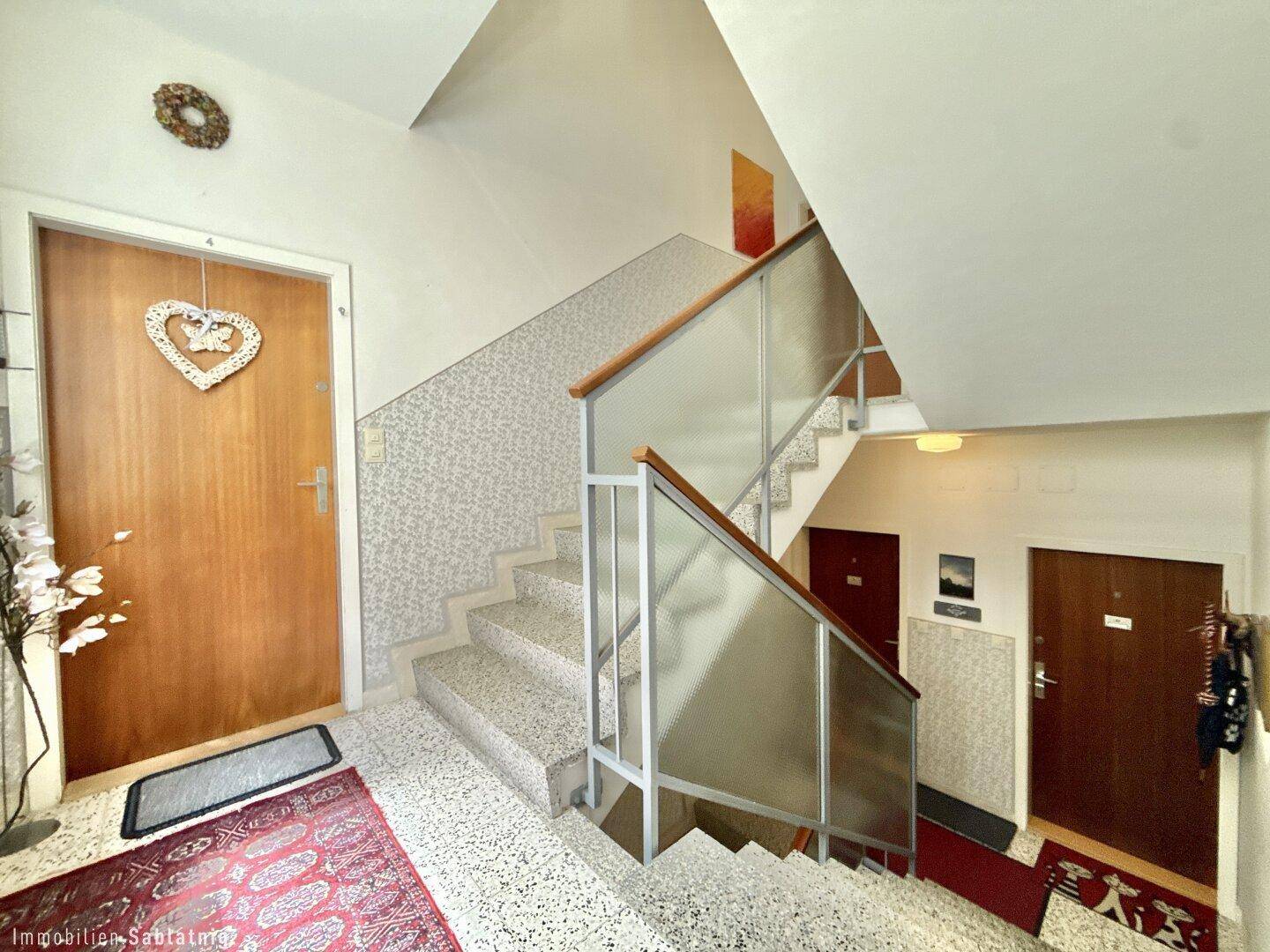 Treppenhaus mit Terrazzoboden, Holzgeländer und Zugang zu den Wohnungen.
