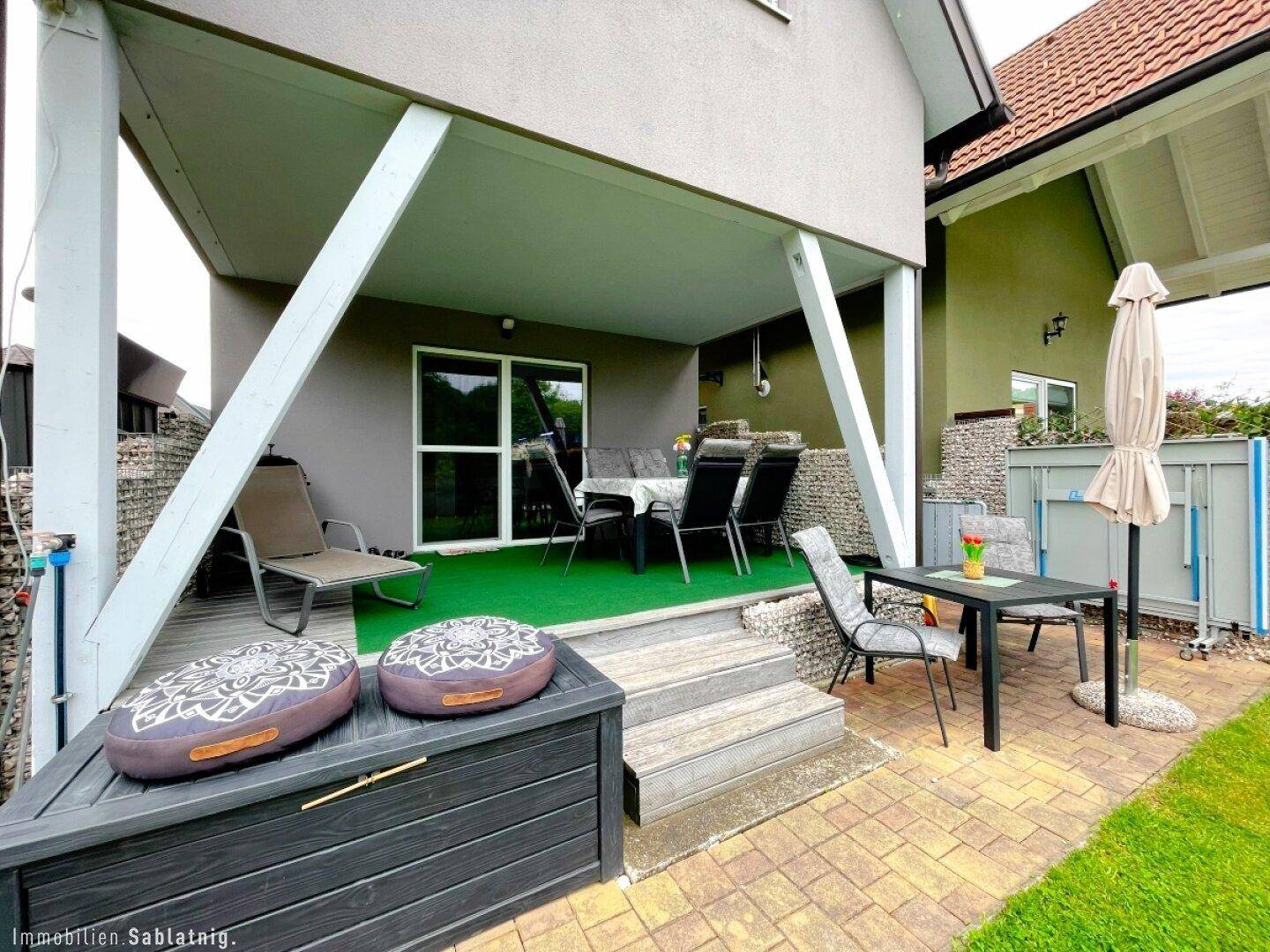 Geräumige überdachte Terrasse mit angrenzendem gepflastertem Bereich und Gartenmöbeln.