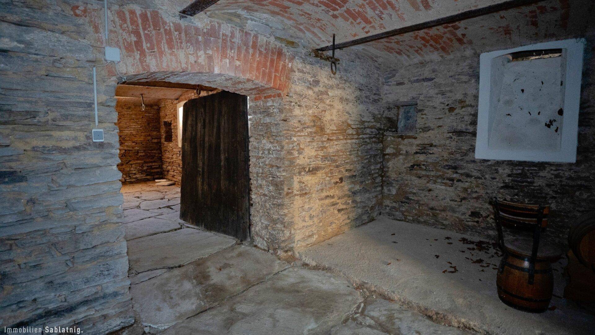 Historischer Keller mit Steinmauern, Holztür und einem kleinen Fenster.