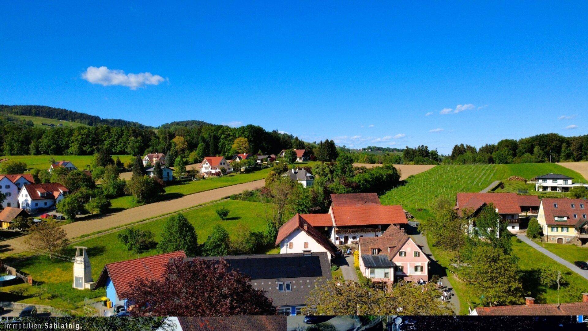 Weitläufige Landschaftsansicht mit Feldern, Wäldern und Häusern unter klarem Himmel.