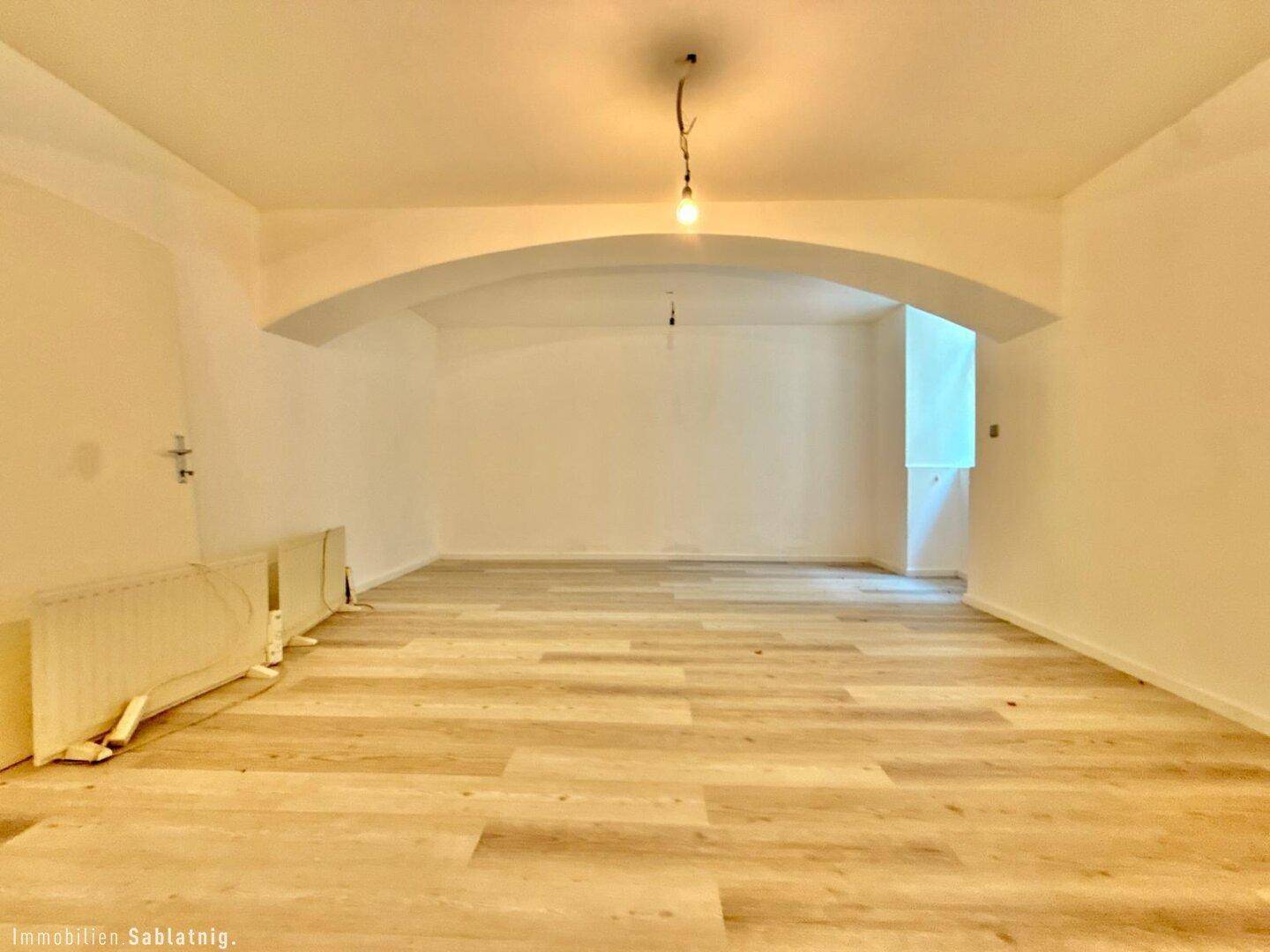 Geräumiger, leerer Raum mit hellem Laminatboden und einer markanten Gewölbedecke, gut beleuchtet.