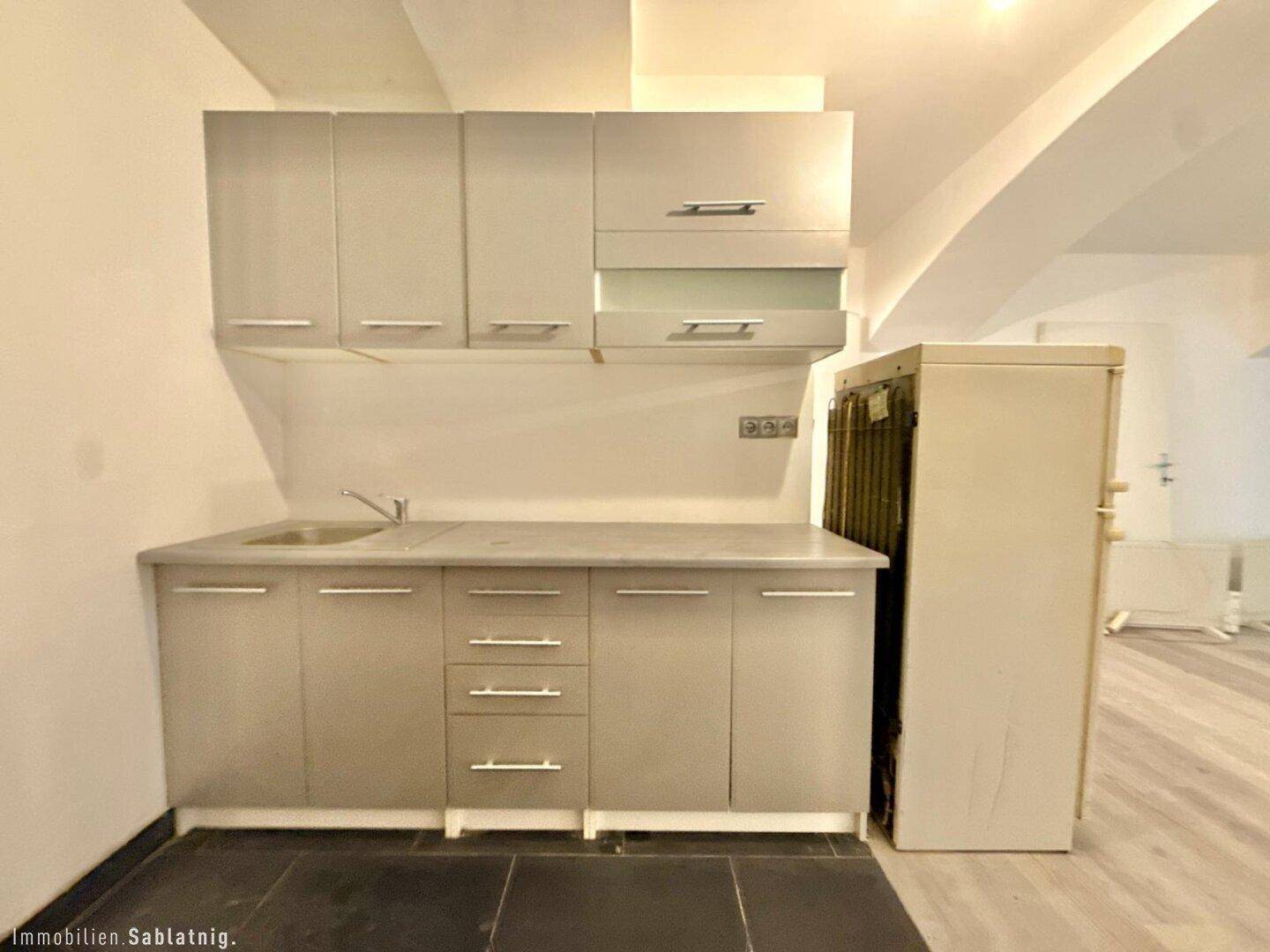 Küchenzeile mit grauen Unterschränken und Hängeschränken, Spüle und einem Kühlschrank daneben.