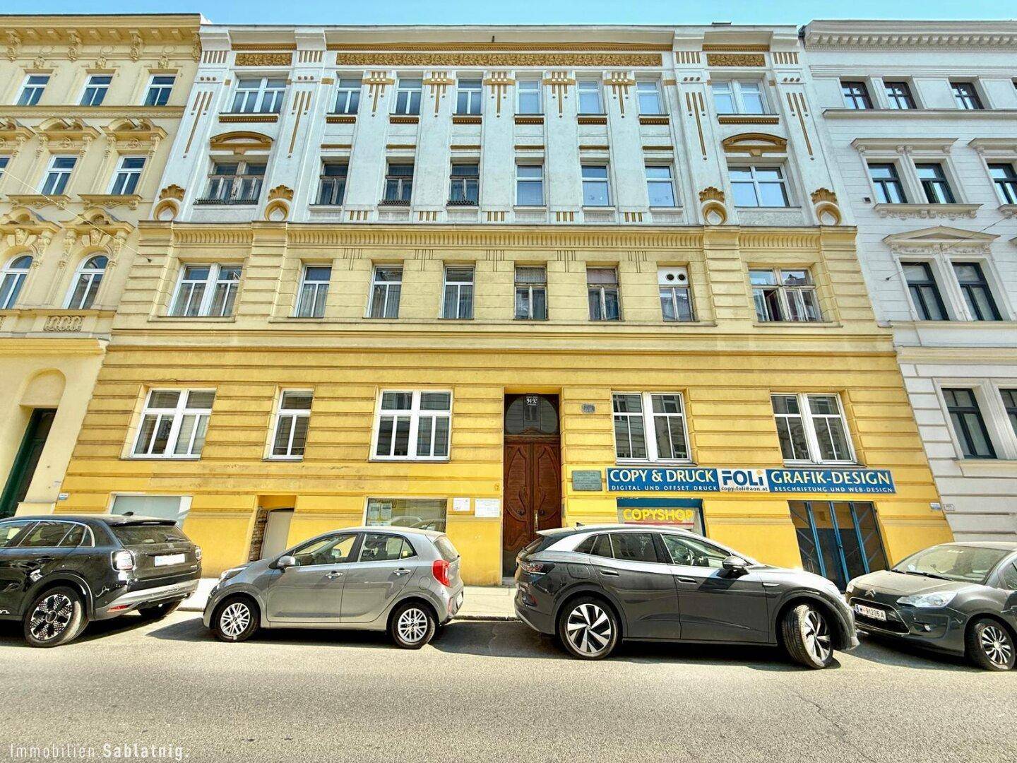 Historisches Wohngebäude mit gelber Fassade und vielen Fenstern, im Erdgeschoss befinden sich Geschäfte.