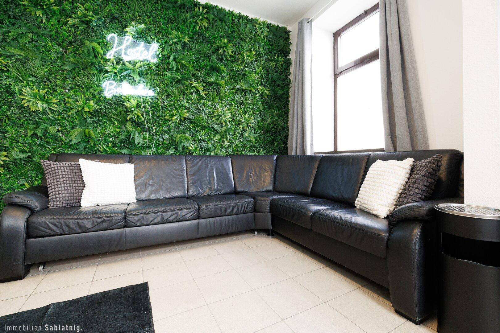 Gemütliche Sitzecke mit einem großen schwarzen Ledersofa und einer grünen Pflanzenwand als Blickfang.