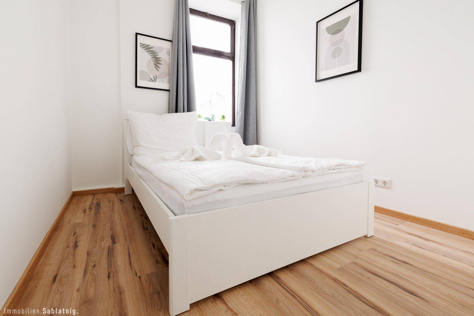 Modernes Schlafzimmer mit weißem Doppelbett, Holzboden und zwei gerahmten Bildern an der Wand.