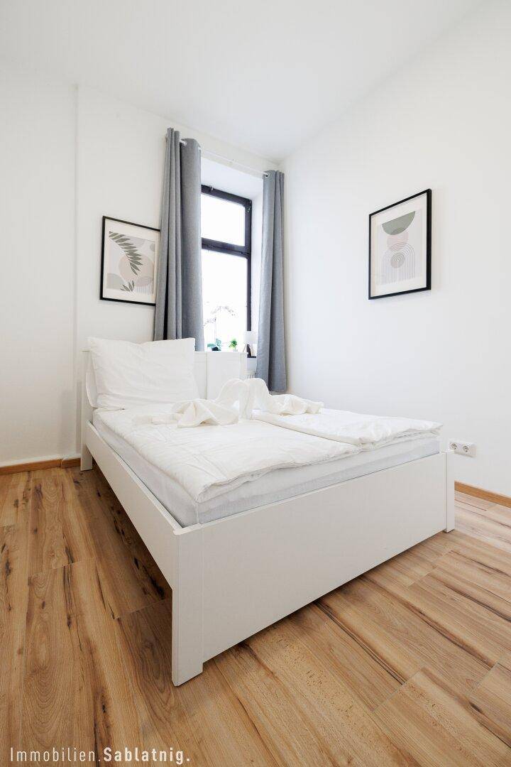 Modernes Schlafzimmer mit weißem Doppelbett, Holzboden und zwei gerahmten Bildern an der Wand.