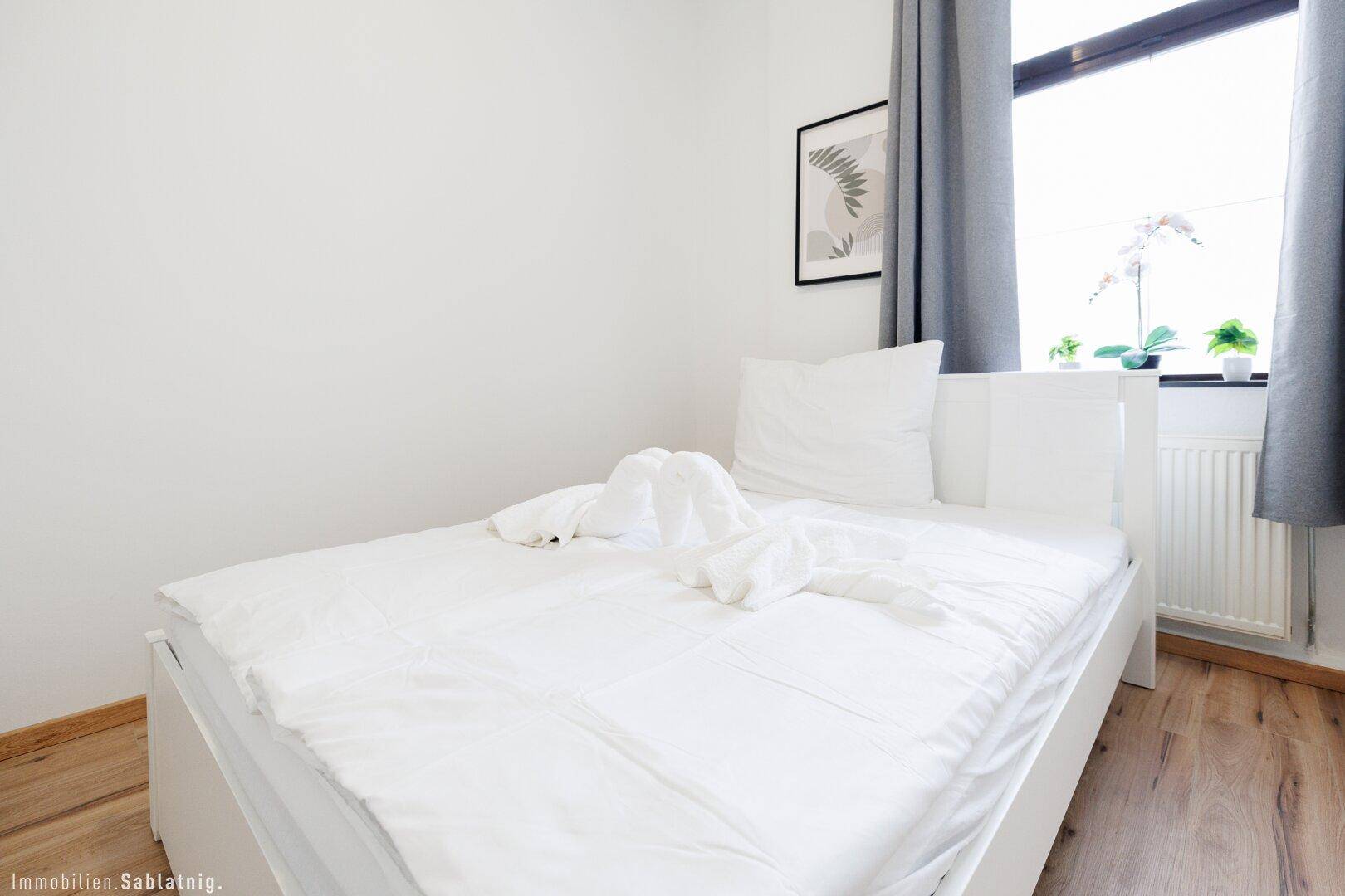 Gemütliches Schlafzimmer mit Einzelbett, Holzboden und einem Fenster mit grauen Vorhängen.